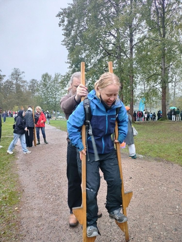 En person står på stylter, og en person hjelper til. 